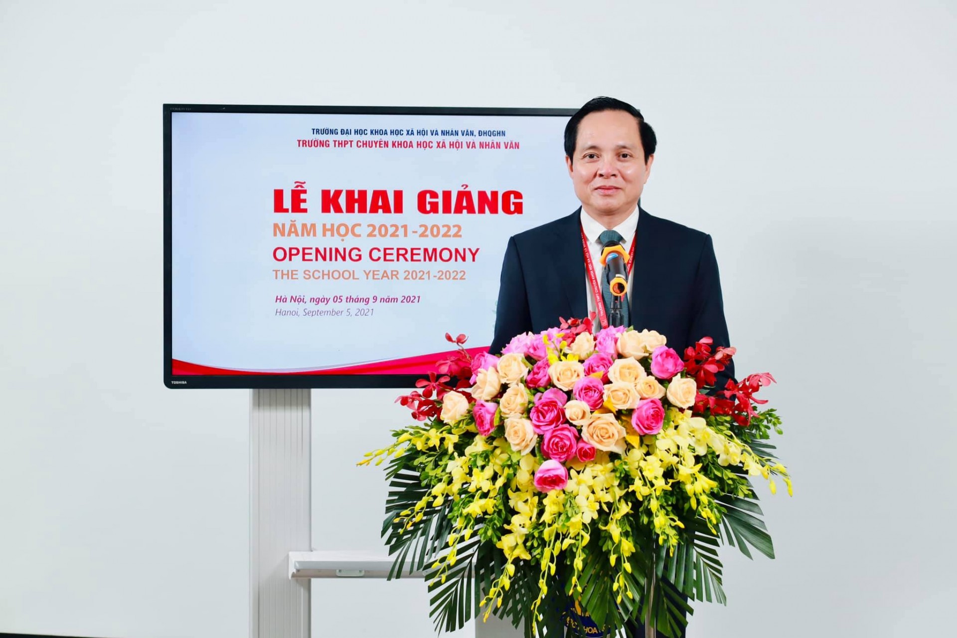 May be an image of 1 person, standing, flower, indoor and text that says 'TRƯỜNG HỘIV ĐHOGHN TRƯỜNG THPT CHUYÊN KHOA AHOIV NHÂN VĂN LỄ KHAI GIẢNG NĂM HỌC 2021-2022 OPENING CEREMONY THE SCHOOL YEAR 2021 -2022 Hà tháng năm 2021 Hanoi, Septembe 2021'